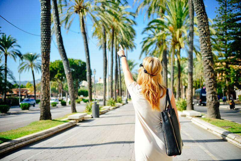 TuGo Traveller with handbag pointing into the distance near palm trees.