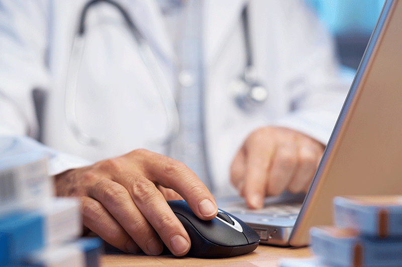 Medical doctor working on his laptop with his right hand resting on the mouse.