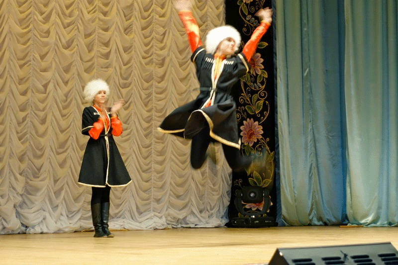 Traditional Russian dancer jumps in the air with arms outstretched while the other claps at a show for travellers.