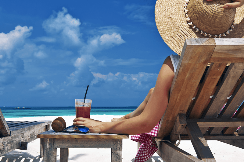 Lady in a wooden reclining chair having a drink at the beach.