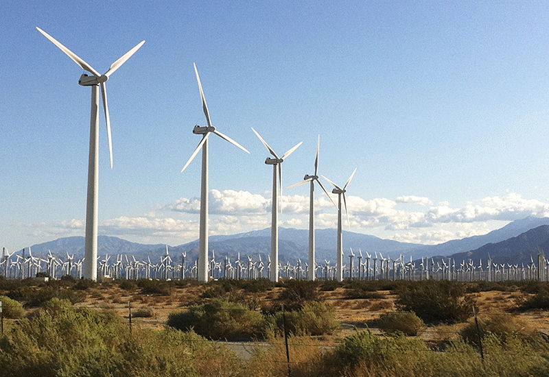 Windmill farm against a scenic backdrop of mountains and blue sky