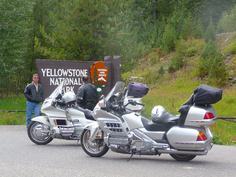 Mark Rovang next to the Yellowstone National Park sign in Wyoming with his motorcycle in the foreground.