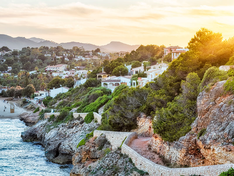 A path winds down to a beach in front homes in Mallorca, Spain, during sunset.