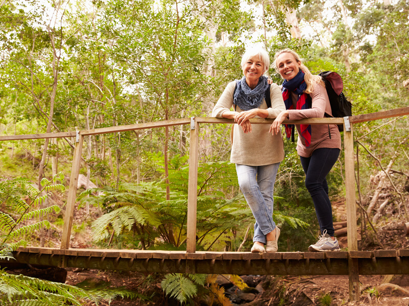 mother and daughter stand on wooden bridge in forest