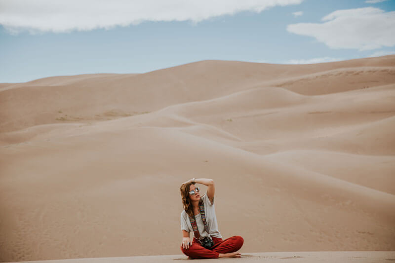 Woman sitting in the desert wearing sun glasses.