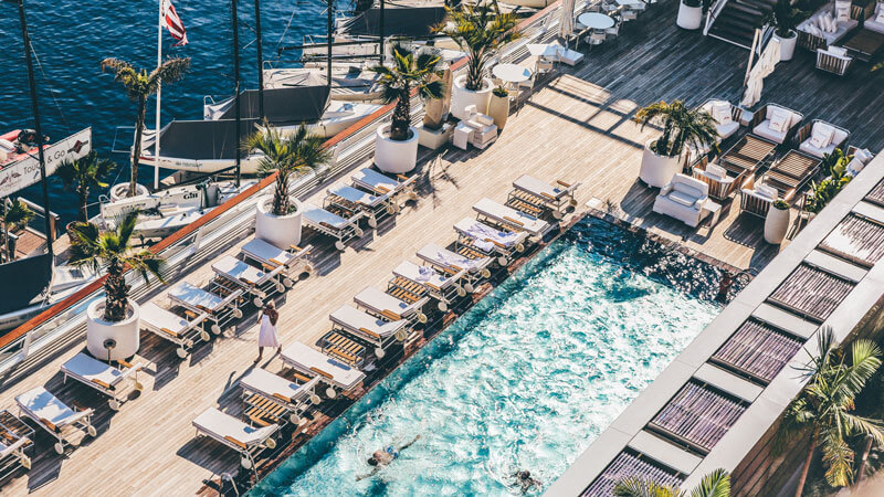 pool on deck by the ocean with deck chairs, palm trees and boats in Monte Carlo, Monaco