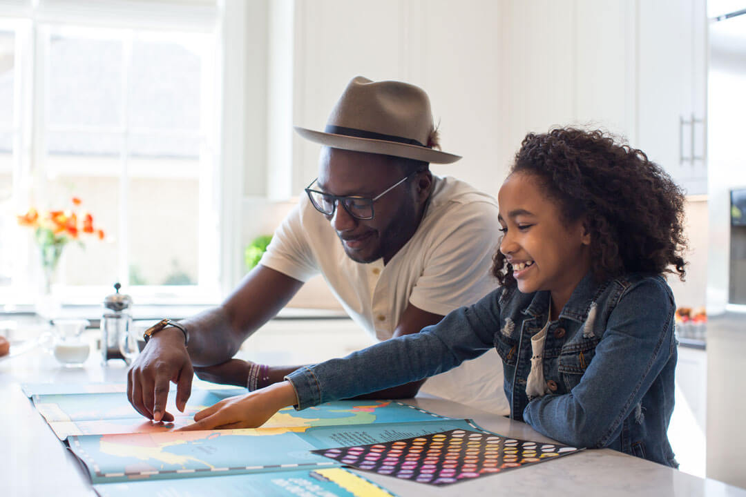 Father and daughter look at map at kitchen counter.