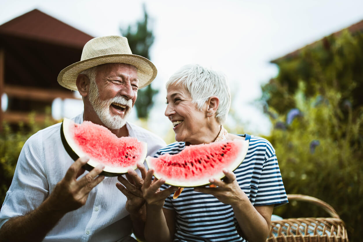 Cheerful senior couple having fun while eating watermelon in the backyard.