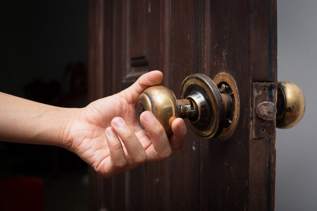 Hand pulling on a broken doorknob on a wooden door.