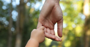 Baby holding the pinky of an adult’s hand in nature