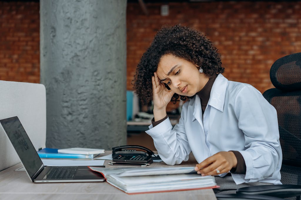 Woman resting her head on her fingers while looking at papers in front of a laptop