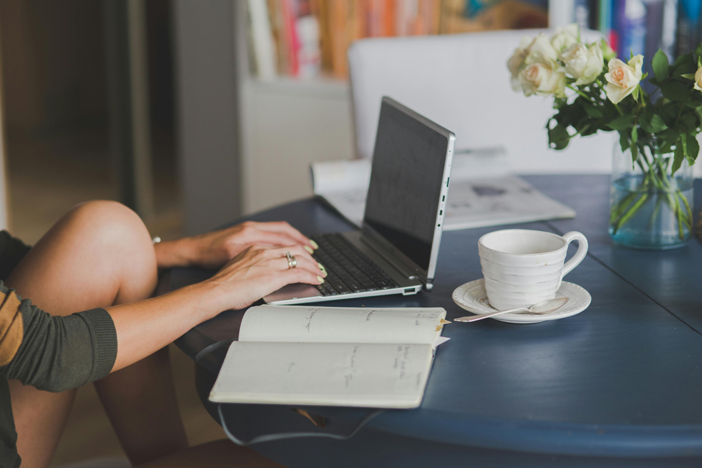 une personne devant son ordinateur avec une tasse à café et des carnets à proximité